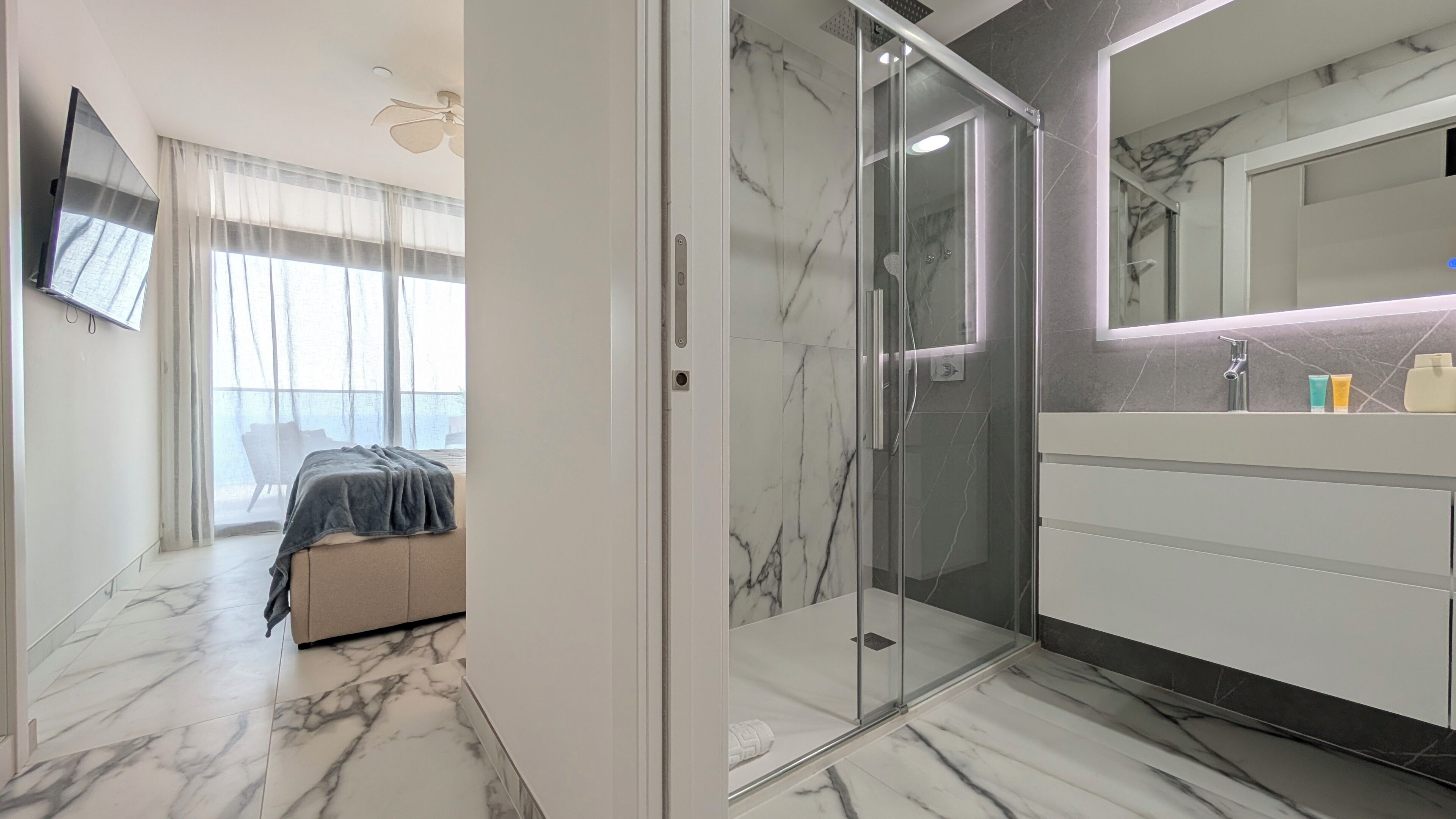 Een moderne badkamer met een douchecabine van glas, een marmeren vloer en een grote spiegel boven de wastafel.