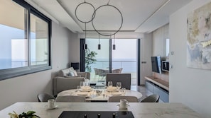 Ein modernes Wohnzimmer mit Essbereich, großen Fenstern, einer Couch und einem Fernseher.
