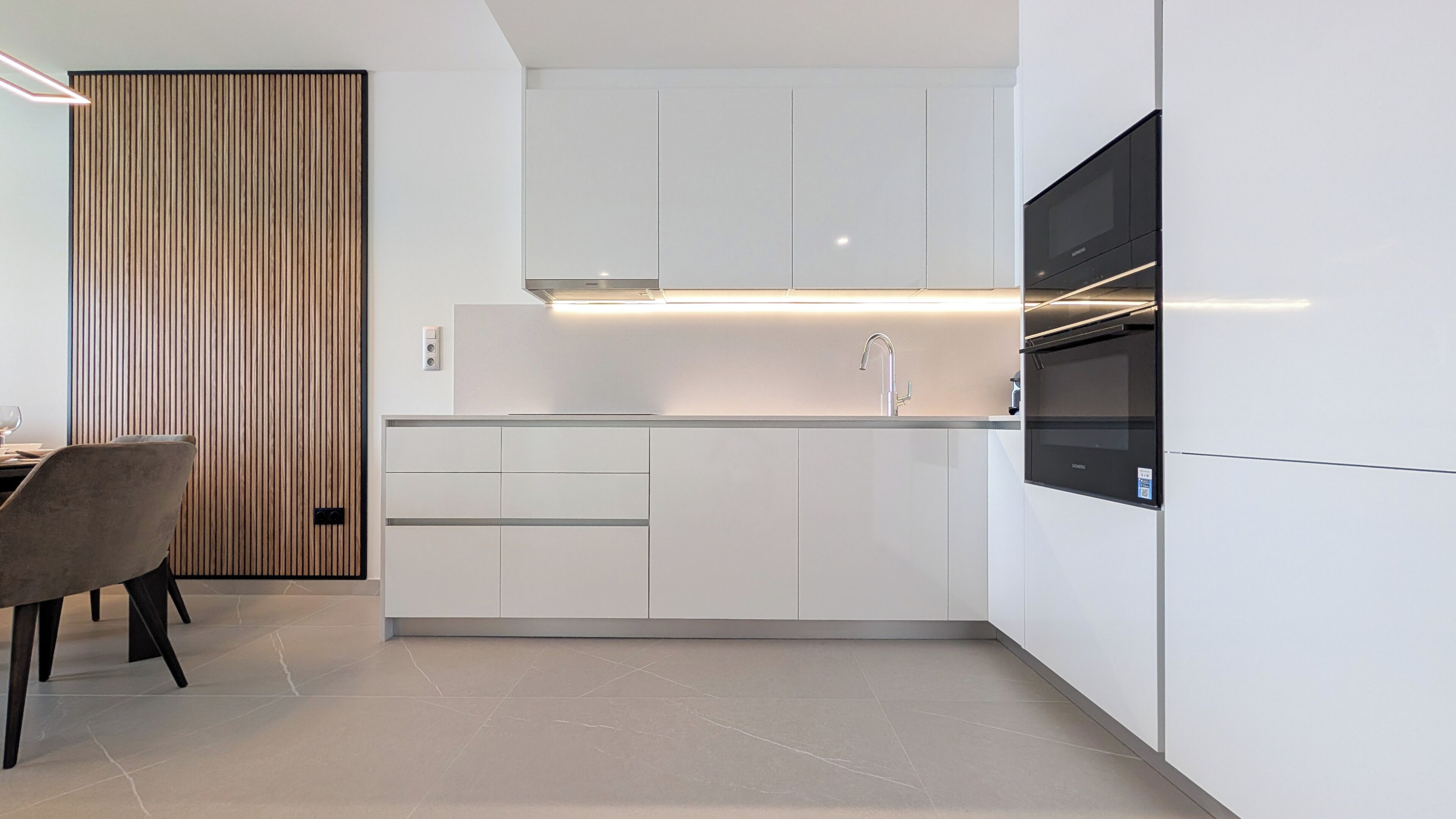 Una cocina moderna con armarios blancos, horno integrado y televisor de pantalla plana.