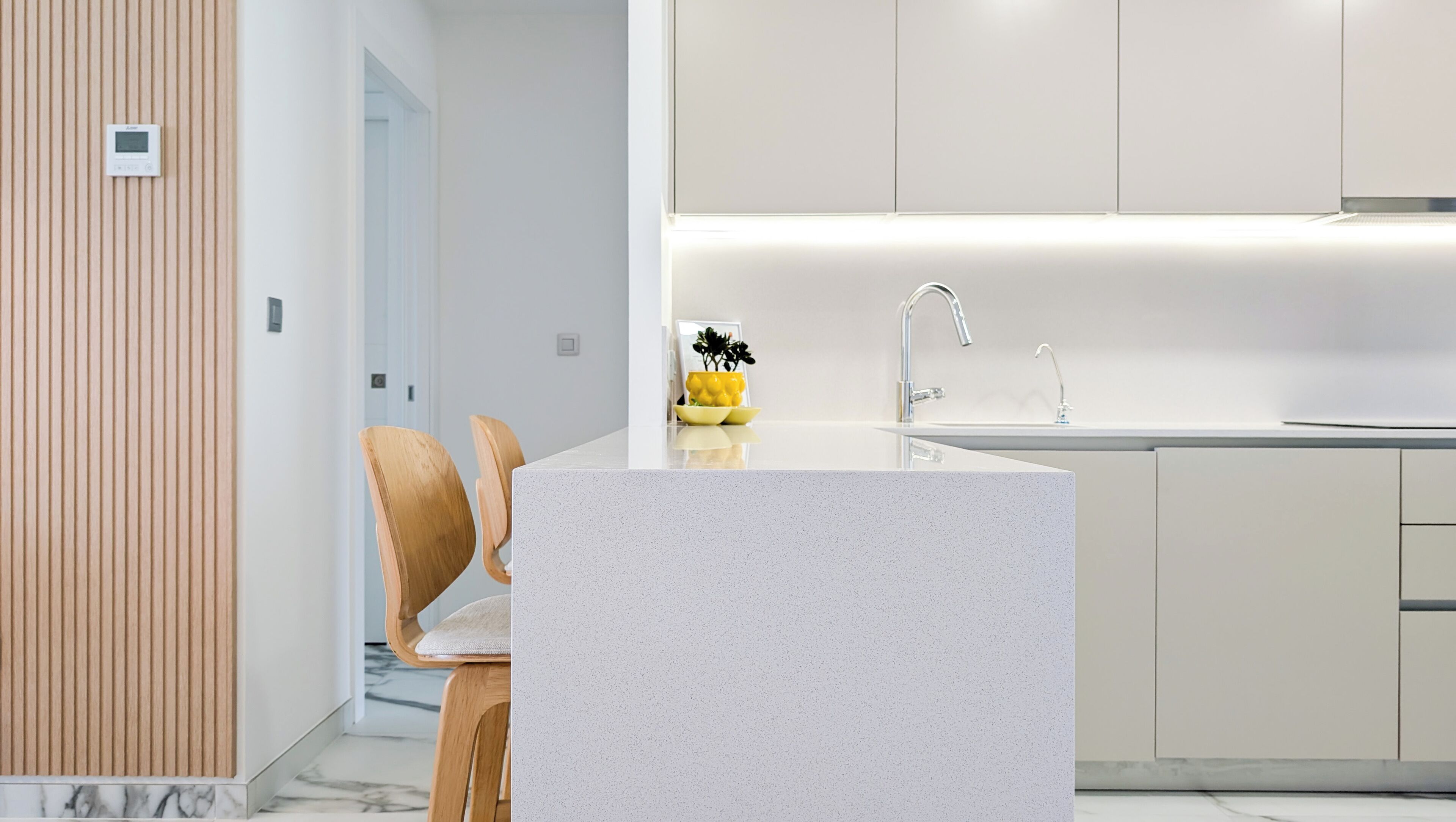 A modern kitchen with a marble countertop, a built-in sink, and wooden chairs.