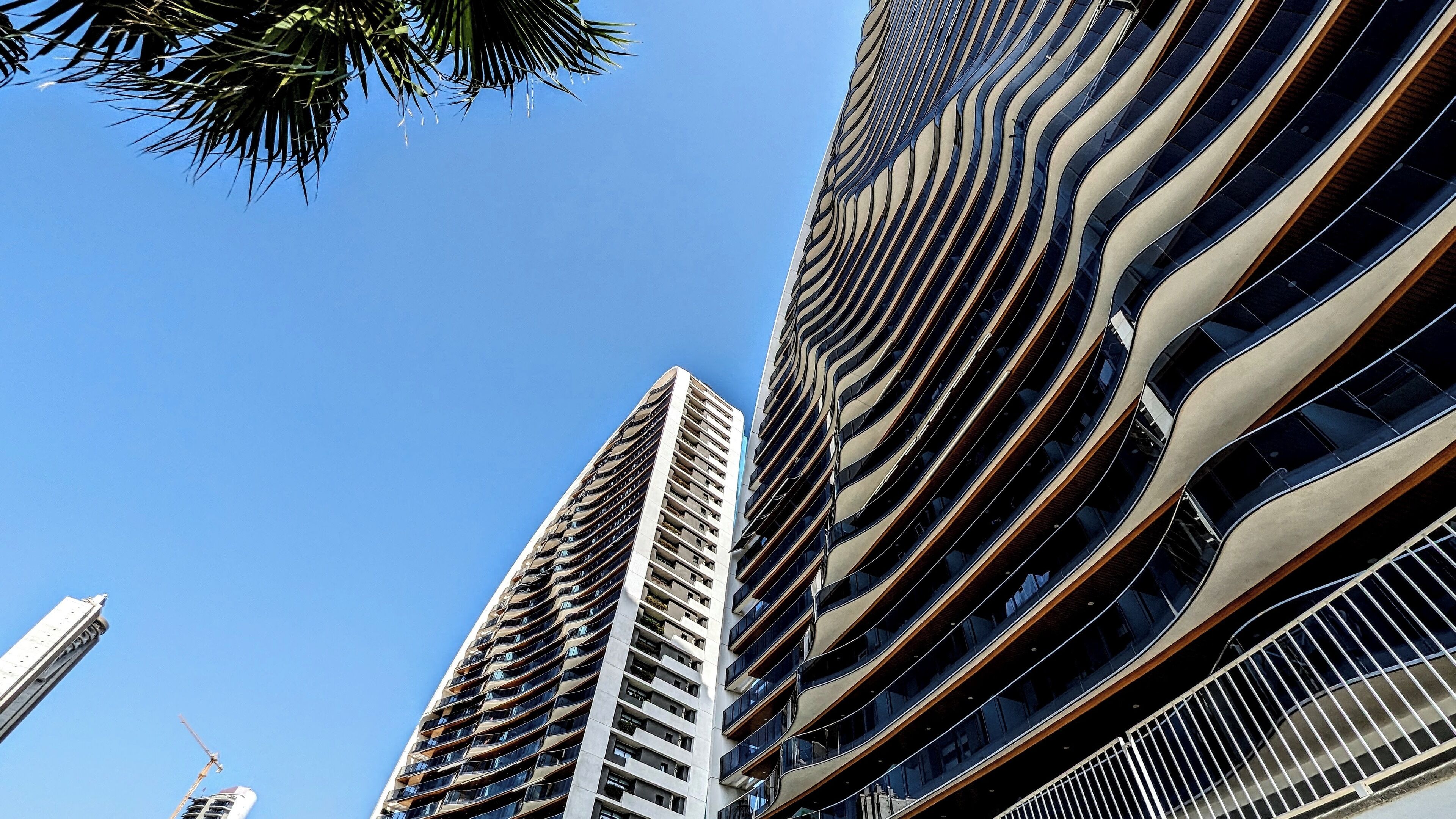 Twee hoge gebouwen met moderne architectuur, met gebogen balkons en reflecterende glazen gevels.
