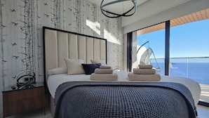 A modern bedroom with a large bed, a hanging chair by the window, and a view of the sea. - Sunset Waves Apartments Tower 1 (Benidorm)