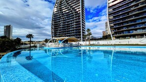 A modern hotel with a large swimming pool, multiple balconies, and a view of the surrounding cityscape. - Sunset Waves Apartments Tower 1 (Benidorm)