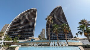 Two high-rise buildings with balconies, a pool area with 'Sunset Waves' signage, and palm trees. - Sunset Waves Apartments Tower 1 (Benidorm)