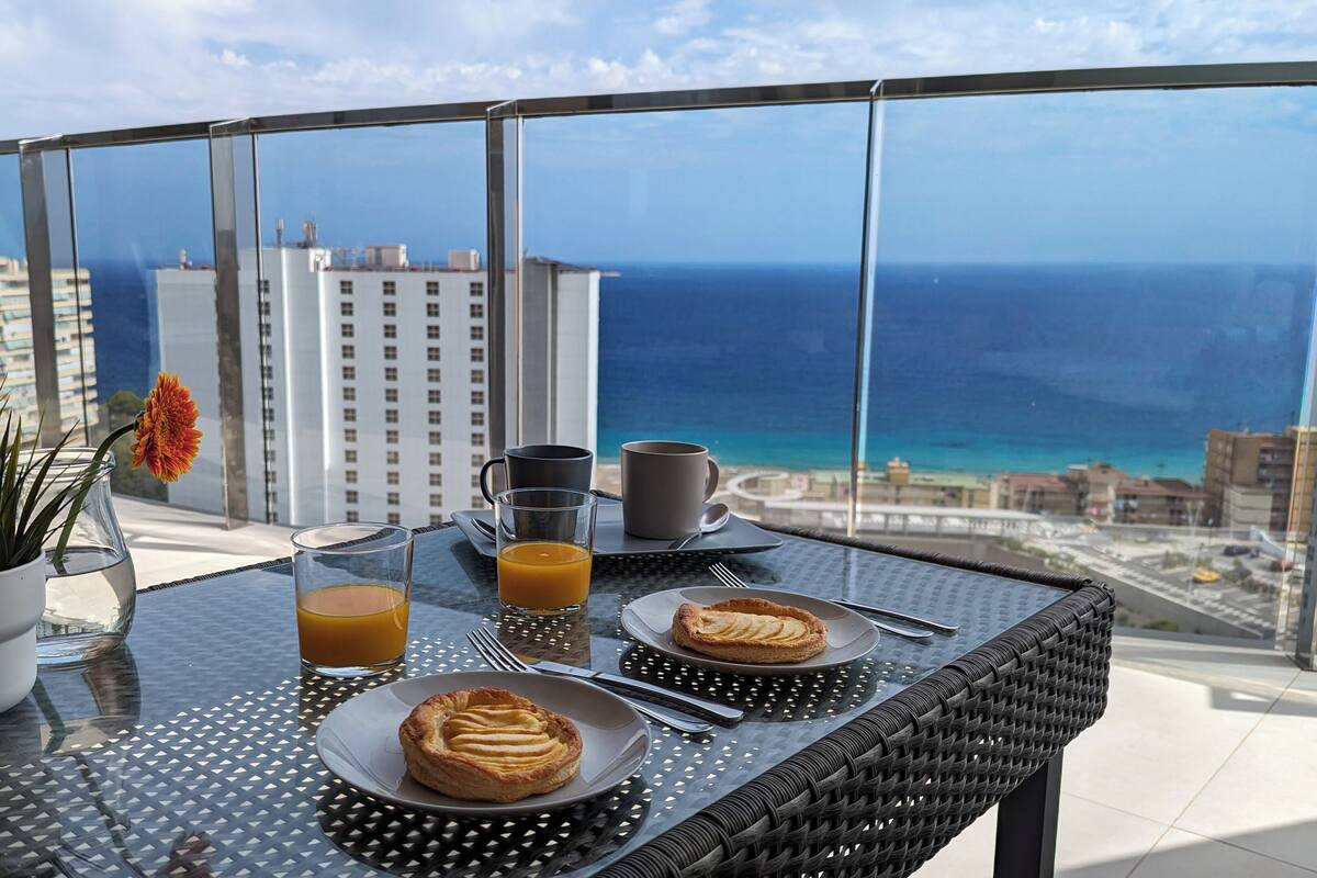 A balcony with a table set for breakfast, including a pastry, a glass of orange juice, and a coffee cup.