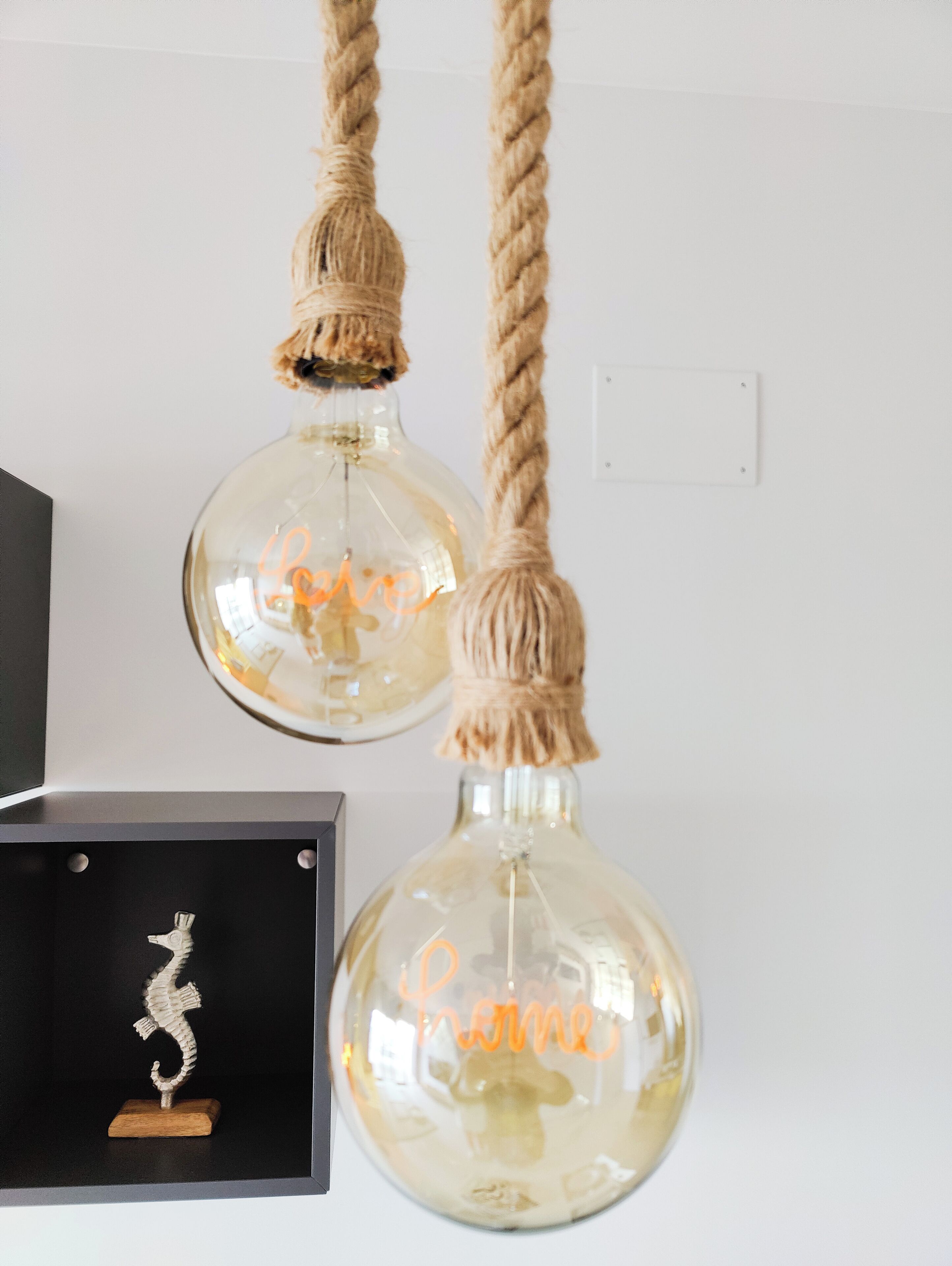 Dos lámparas de cristal esféricas con asas de cuerda, una con la palabra 'Love' y la otra con la palabra 'Home' escritas en su interior.