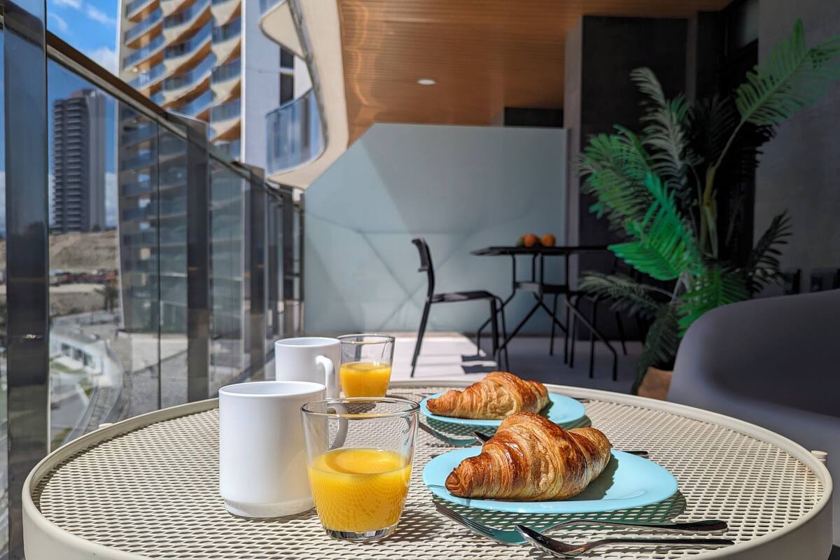 A balcony with a table set for breakfast, including croissants, a glass of orange juice, and a white mug.