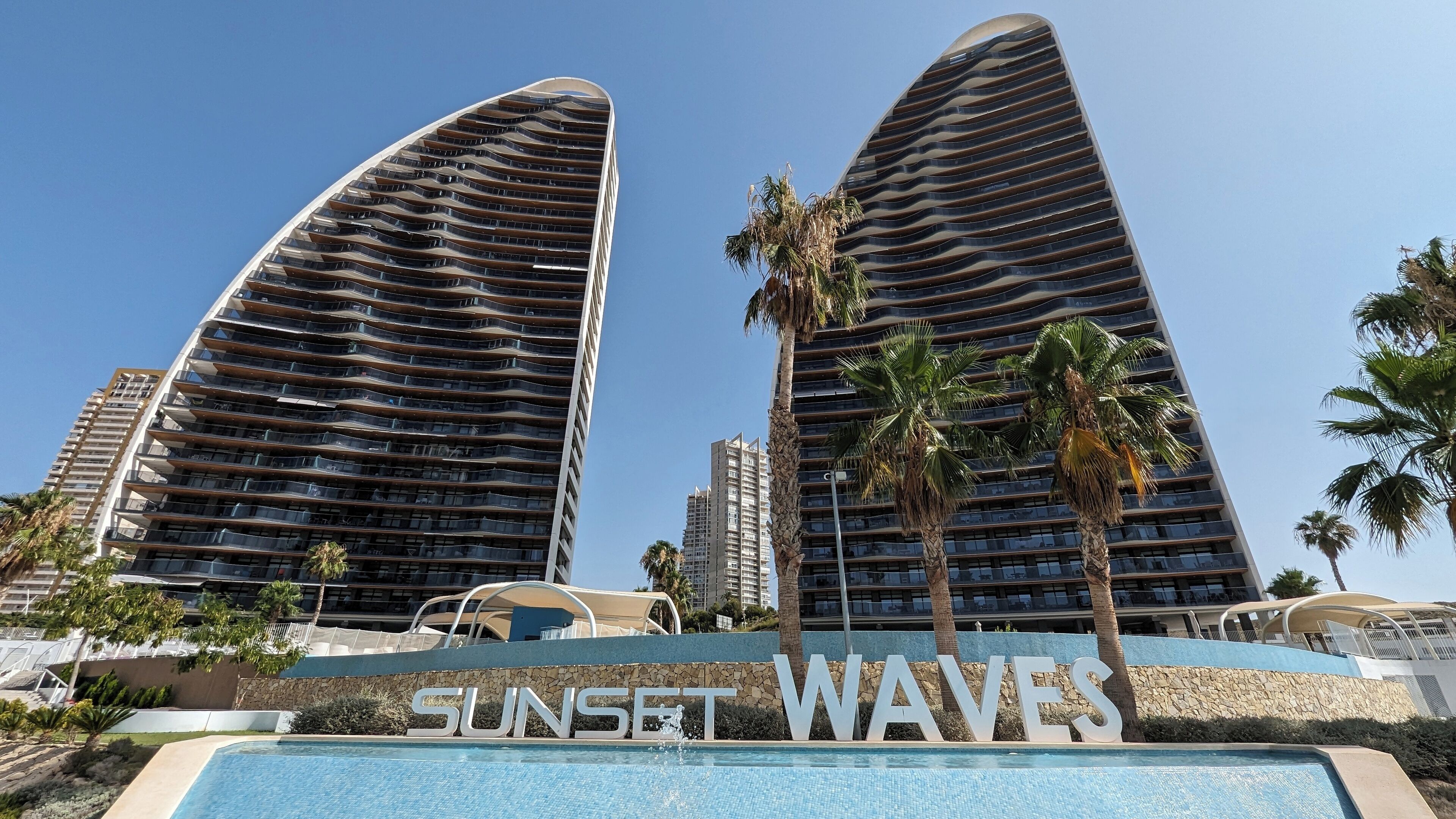 A modern hotel with a unique curved architecture, a pool area, and the name 'Sunset Waves' prominently displayed.