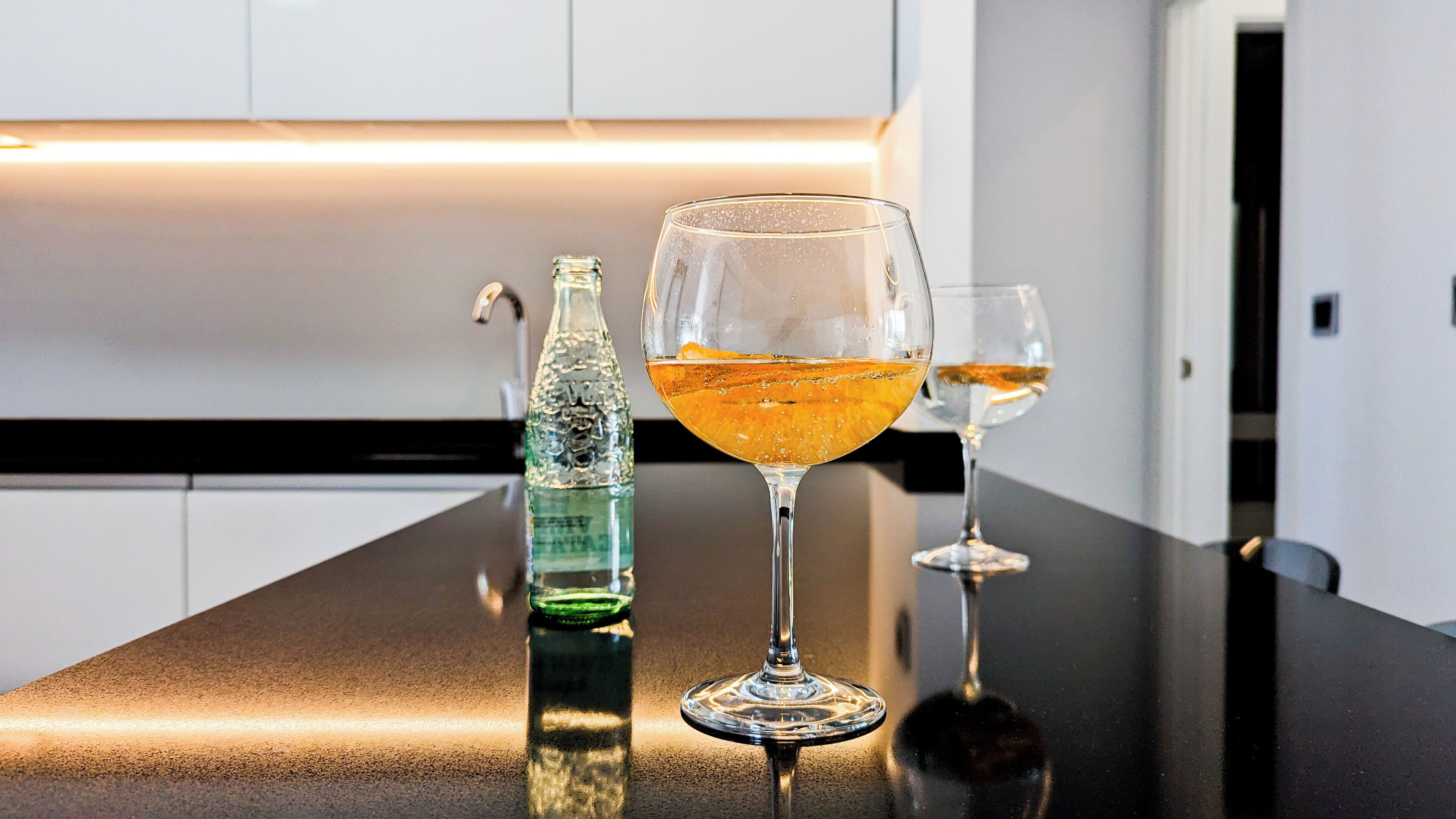 En bardisk med en vattenflaska och två glas med en gyllene dryck stående på en blank bänkskiva.