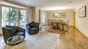 Een ruime woonkamer met een groot raam, een eethoek met een houten tafel en stoelen, en een decoratieve boom.