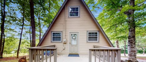 A wooden cabin with a front porch, two windows, and a door with a wreath.