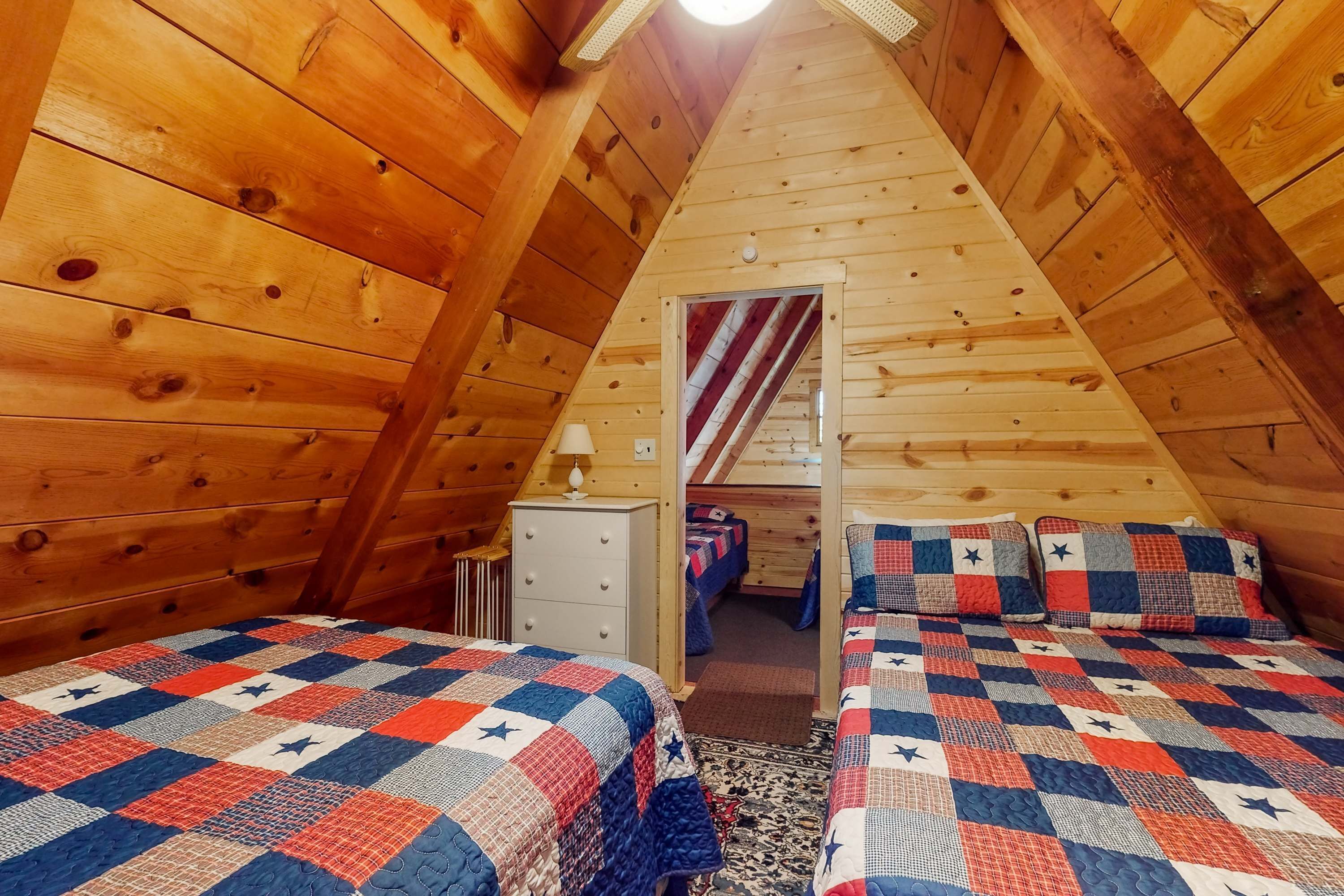 Ein gemütliches Schlafzimmer im Dachgeschoss mit Holzwänden, zwei Betten mit Sterndecken und einem kleinen Schminktisch sowie einer Lampe.