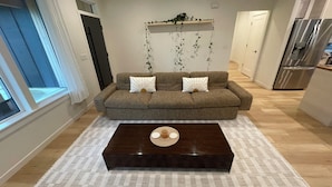 Un salon avec un canapé marron, deux coussins décoratifs, une table basse en bois foncé et un tapis à motifs.
