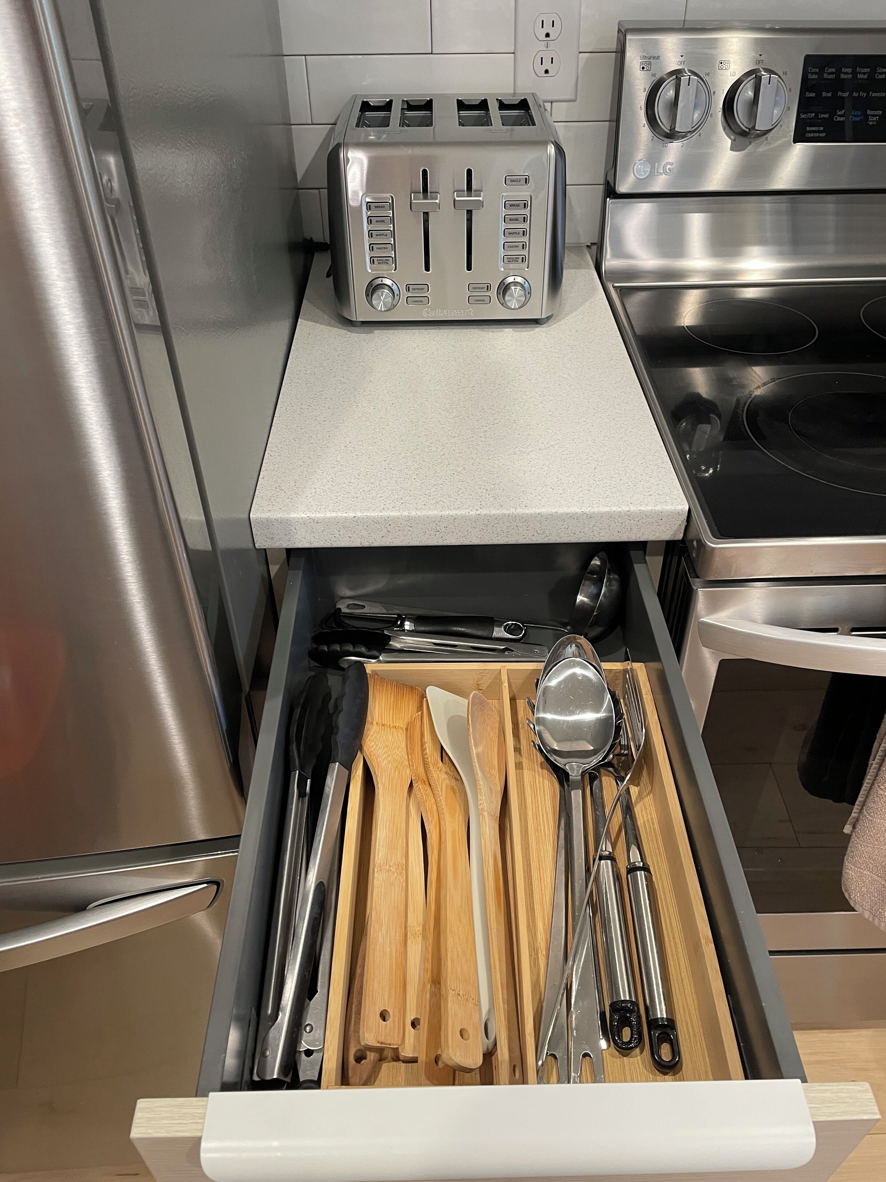 A kitchen with a stainless steel toaster, a microwave, and a drawer containing wooden utensils.