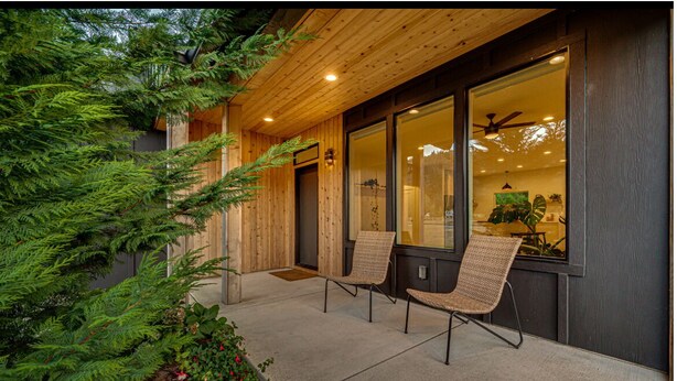 Un bâtiment moderne doté d’une façade en bois, de grandes fenêtres et d’un espace extérieur aménagé avec des sièges.