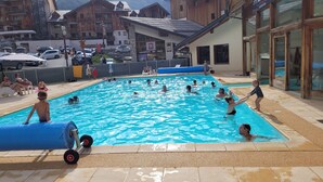 A swimming pool area with people swimming and playing, surrounded by buildings and a parking area. - Apartment 36 M2 6 persons Orres 1800 (Les Orres)