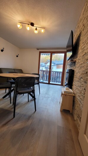 A spacious living area with a wooden dining table, black chairs, a fireplace, and a large sliding glass door leading to a balcony. - Apartment 36 M2 6 persons Orres 1800 (Les Orres)