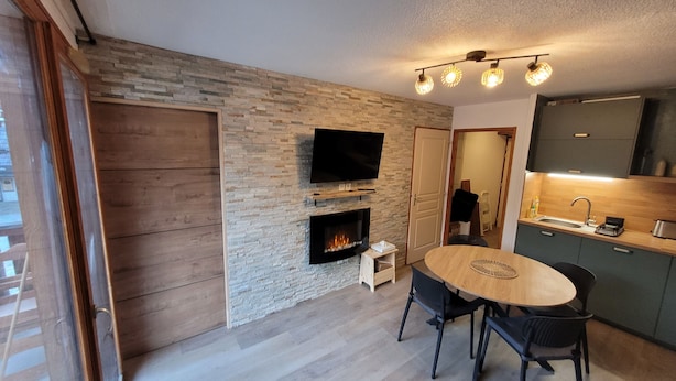 A modern kitchen with a flat-screen TV, a fireplace, and a dining area with a round table and chairs. - Apartment 36 M2 6 persons Orres 1800 (Les Orres)
