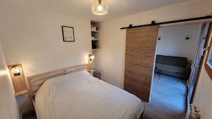 A bedroom with a bed, bedside lamps, a wooden wardrobe, a framed picture on the wall, and a sofa in the adjacent room. - Apartment 36 M2 6 persons Orres 1800 (Les Orres)