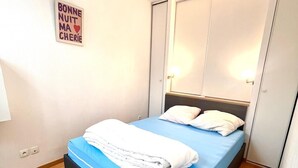 Ein ordentlich bezogenes Bett mit blauer Matratze und weißer Bettwäsche, eine Nachttischlampe und ein Schild an der Wand.