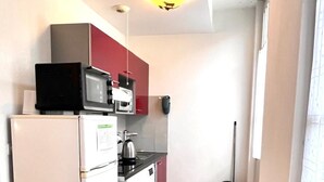 Eine kleine Küche mit Kühlschrank, Mikrowelle und Herd, Holzboden und einem Fenster mit Jalousien.