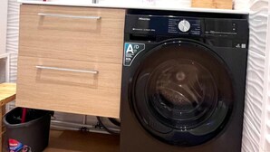 Ein kleines, modernes Badezimmer mit integrierter Waschmaschine, einem Holzwaschtisch mit Spiegel und einem kleinen Mülleimer.