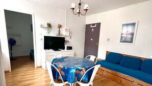 Ein modernes Wohnzimmer mit Esstisch, weißen Stühlen, einem blauen Sofa und einem Fernseher.