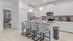 A modern kitchen with white cabinets, a central island with bar stools, stainless steel appliances, and pendant lighting. - Near Disney Villa: Private Pool & Game Room (Davenport)