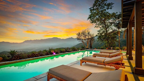 Una piscina a sfioro con lettini prendisole, immersa nel verde e con vista sulle montagne lontane.