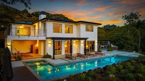 Una moderna casa a due piani con piscina, area relax esterna e vista sul paesaggio circostante.