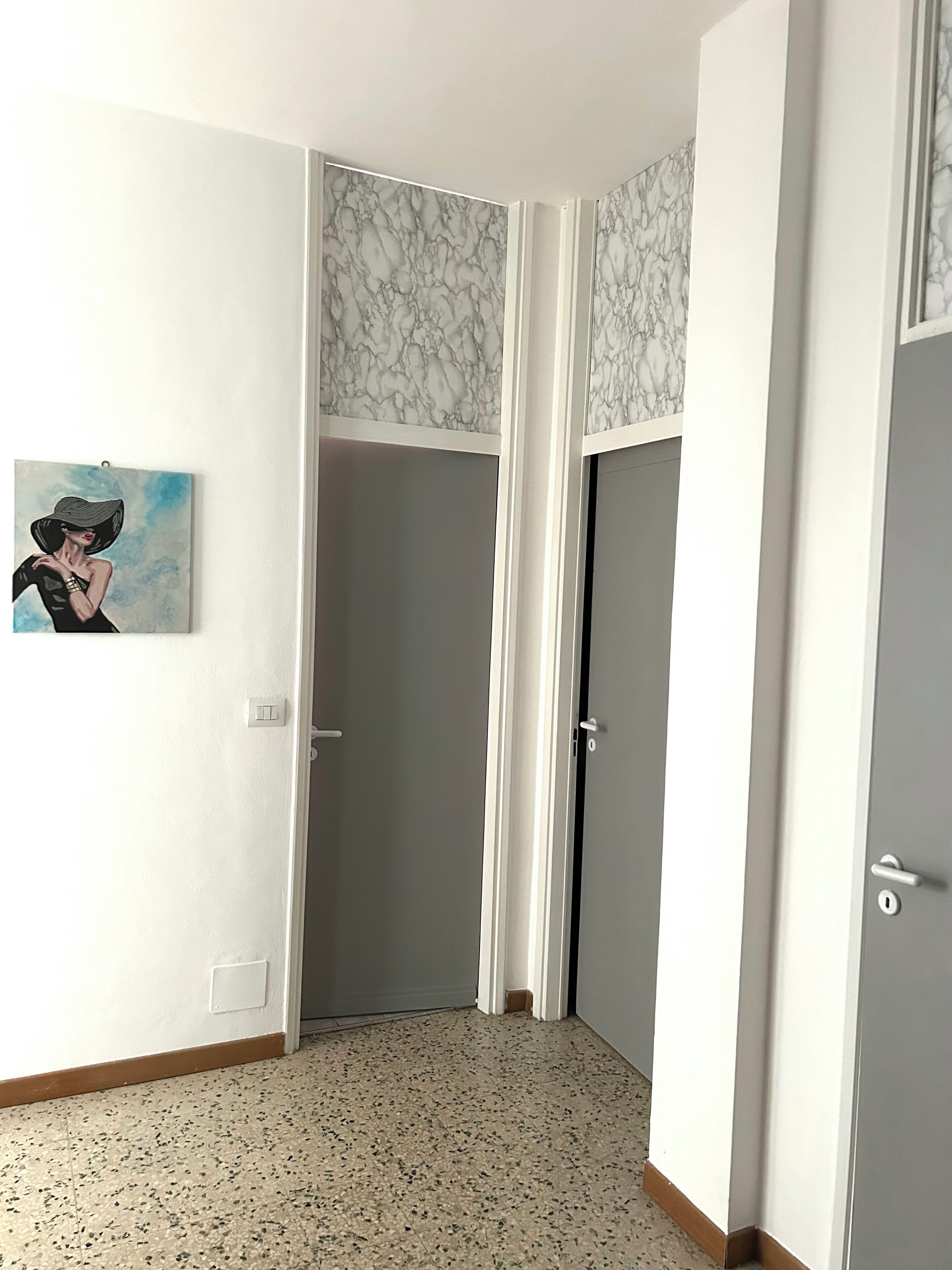 Un couloir avec un mur décoré d’un motif imitant le marbre, une porte et un tableau représentant une femme.