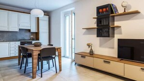 A modern kitchen with white cabinets, a wooden dining table, and a TV on a wooden stand. - Celia's house near Bellagio (Lezzeno)