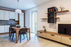 A modern kitchen with white cabinets, a wooden dining table, and a TV on a wooden stand. - Celia's house near Bellagio (Lezzeno)