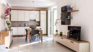 A modern kitchen with white cabinets, a dining area with a table and chairs, a TV on a wooden stand, and a small shelf with decorative items. - Celia's house near Bellagio (Lezzeno)