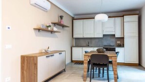 A compact kitchen with white cabinets, a wooden dining table, and a hanging pendant light. - Celia's house near Bellagio (Lezzeno)