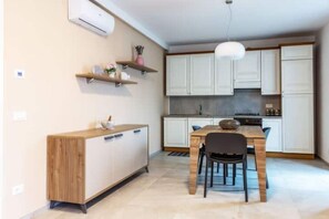 A compact kitchen with white cabinets, a wooden dining table, and a hanging pendant light. - Celia's house near Bellagio (Lezzeno)