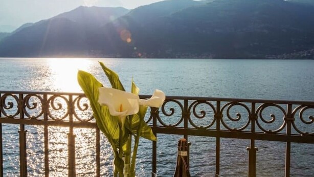 A balcony with a view of a lake and mountains, a bottle of champagne, and a white decorative object. - Celia's house near Bellagio (Lezzeno)