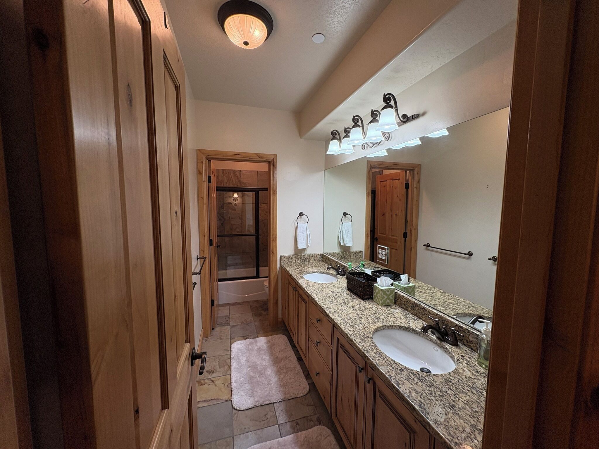 A bathroom with wooden cabinets, a double sink, a large mirror, and a shower area.