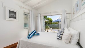 A bedroom with a bed, white curtains, a framed picture, and a view of the outdoors. - Hummingbird Villa (Porters)