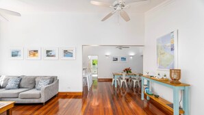 A modern living room with a grey sofa, wooden flooring, a dining area with a table and chairs, and a ceiling fan. - Hummingbird Villa (Porters)