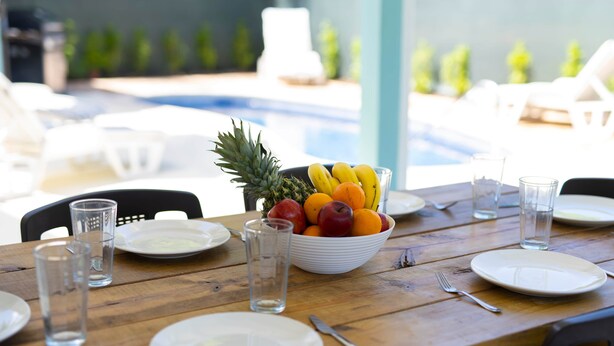 A dining table with plates, cutlery, glasses, and a bowl of fruit. - Hummingbird Villa (Porters)