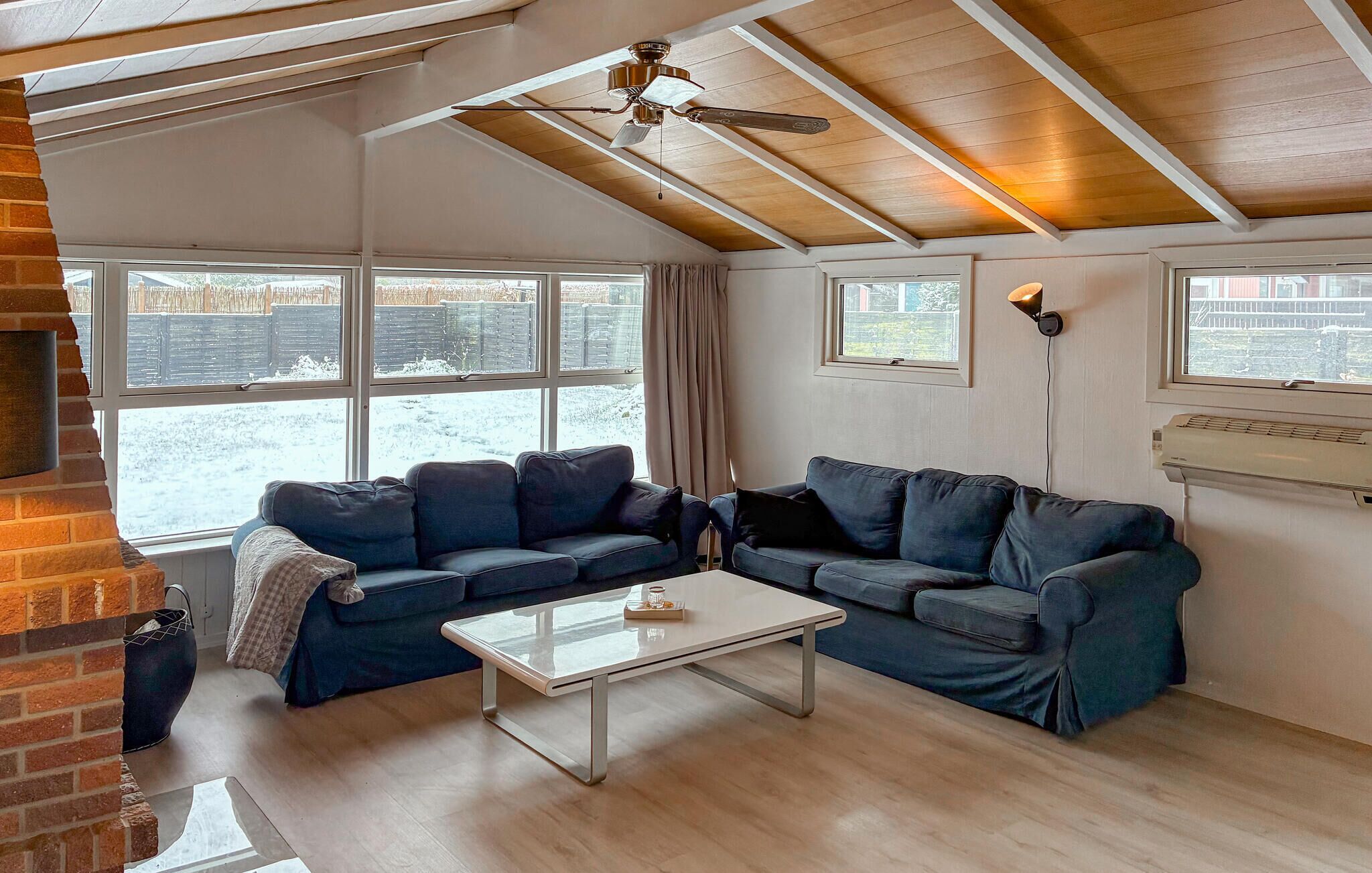 A cozy living room with a brick fireplace, two dark blue sofas, a white coffee table, and a ceiling fan.