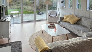 Ein großzügiges Wohnzimmer mit einer Couch, einem Couchtisch und einem Sessel. Ein großes Fenster bietet Blick ins Freie.