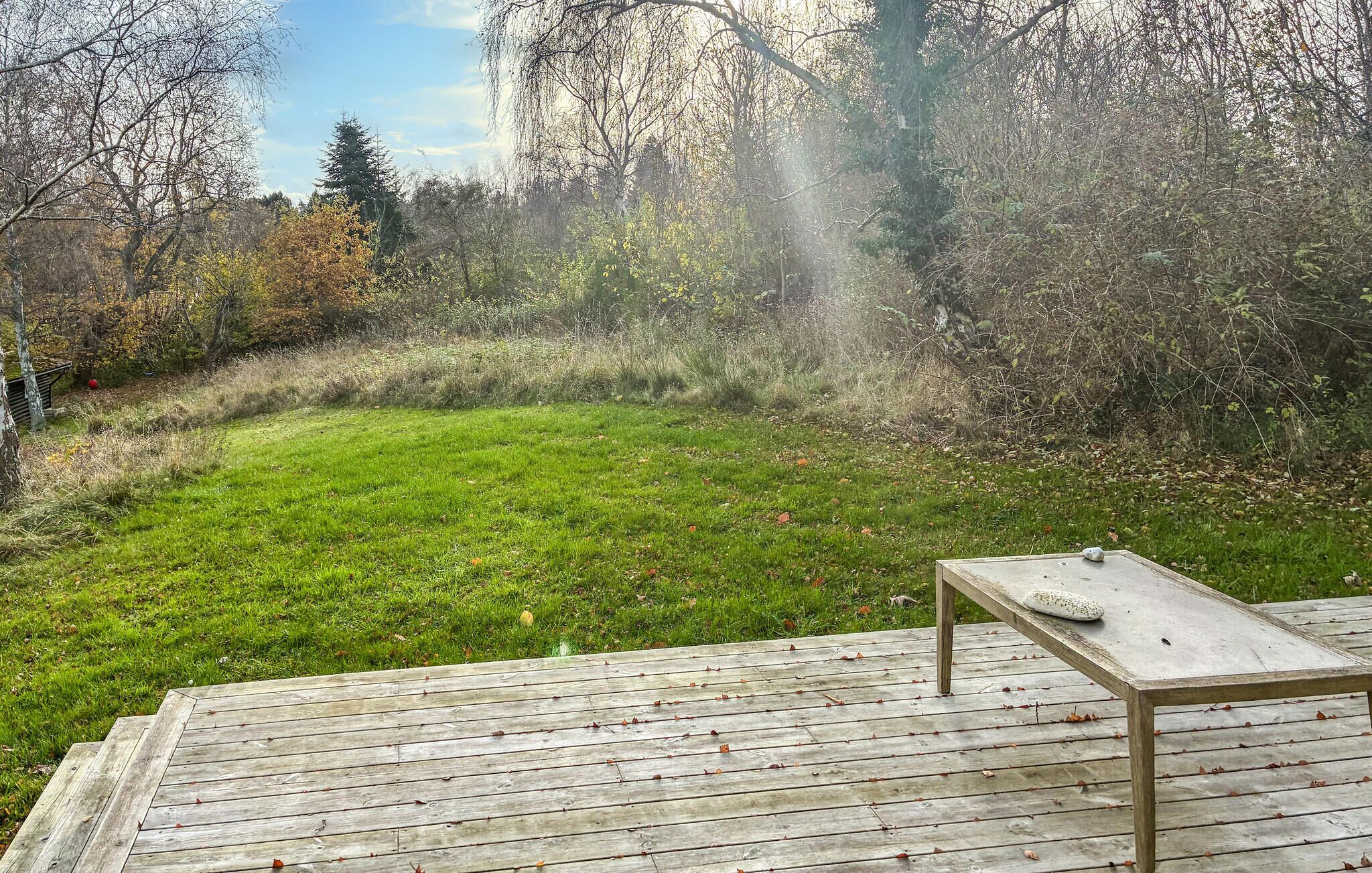 Una terraza de madera con una mesa y sillas, rodeada de césped y árboles.