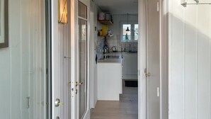 Ein schmaler Flur führt zu einer Küche mit weißen Schränken, einem Fenster und einer Tür mit Messinggriffen.
