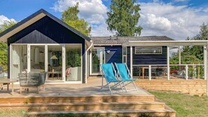 Ein modernes Haus mit Terrasse, einem Wintergarten und einer Außenterrasse mit Sitzgelegenheiten.