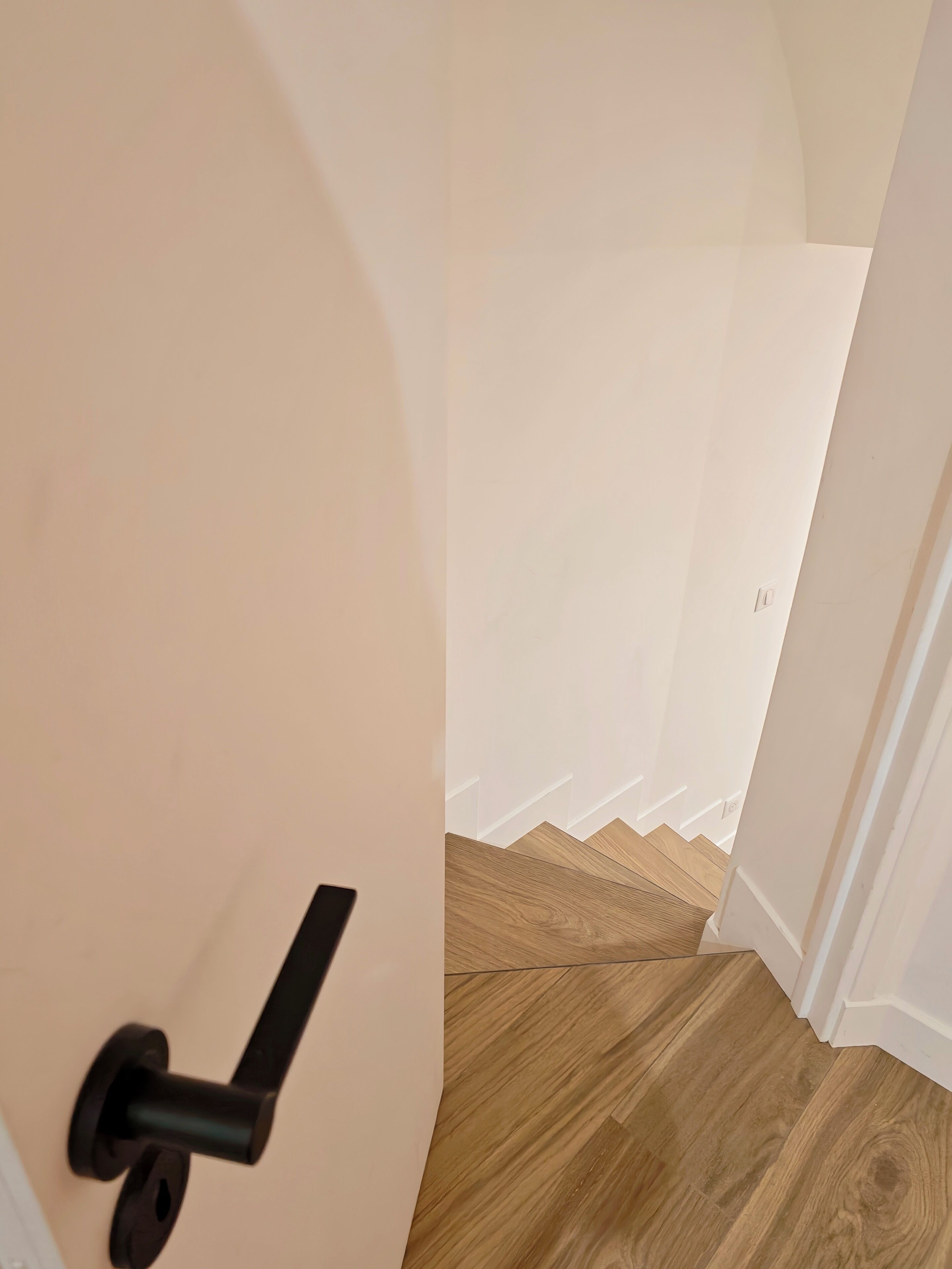 A hallway with a wooden floor and a door with a black handle.