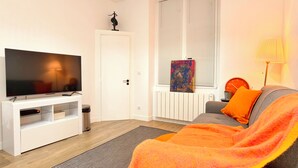 Un soggiorno moderno con una televisione a schermo piatto, un divano, una coperta e un quadro appeso al muro.