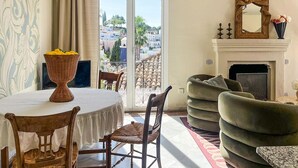 Ein Zimmer mit Esstisch, Stühlen, einer Couch, einem Kamin und Blick auf eine Stadtlandschaft durch ein großes Fenster.