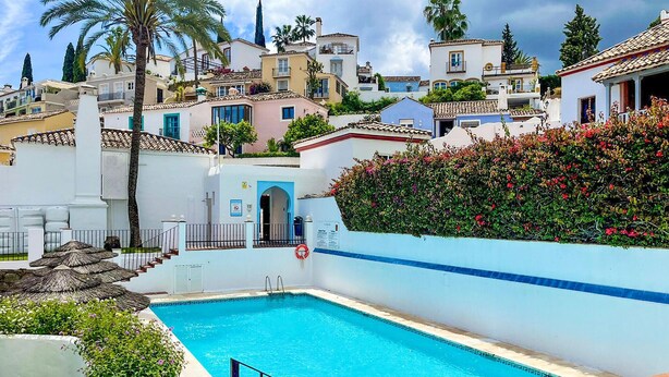 Ein Swimmingpool mit blauer Umrandung, umgeben von weißen Wänden und einer Hecke mit roten Blüten.